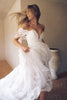 A woman wearing a white off-the-shoulder lace wedding gown with a deep V neckline and a full layered skirt_XS_