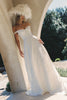 A woman wearing an off-the-shoulder white wedding dress with a fitted bodice and flowing skirt_XS_