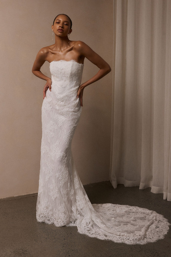 A woman wearing a strapless white lace wedding gown with a long train