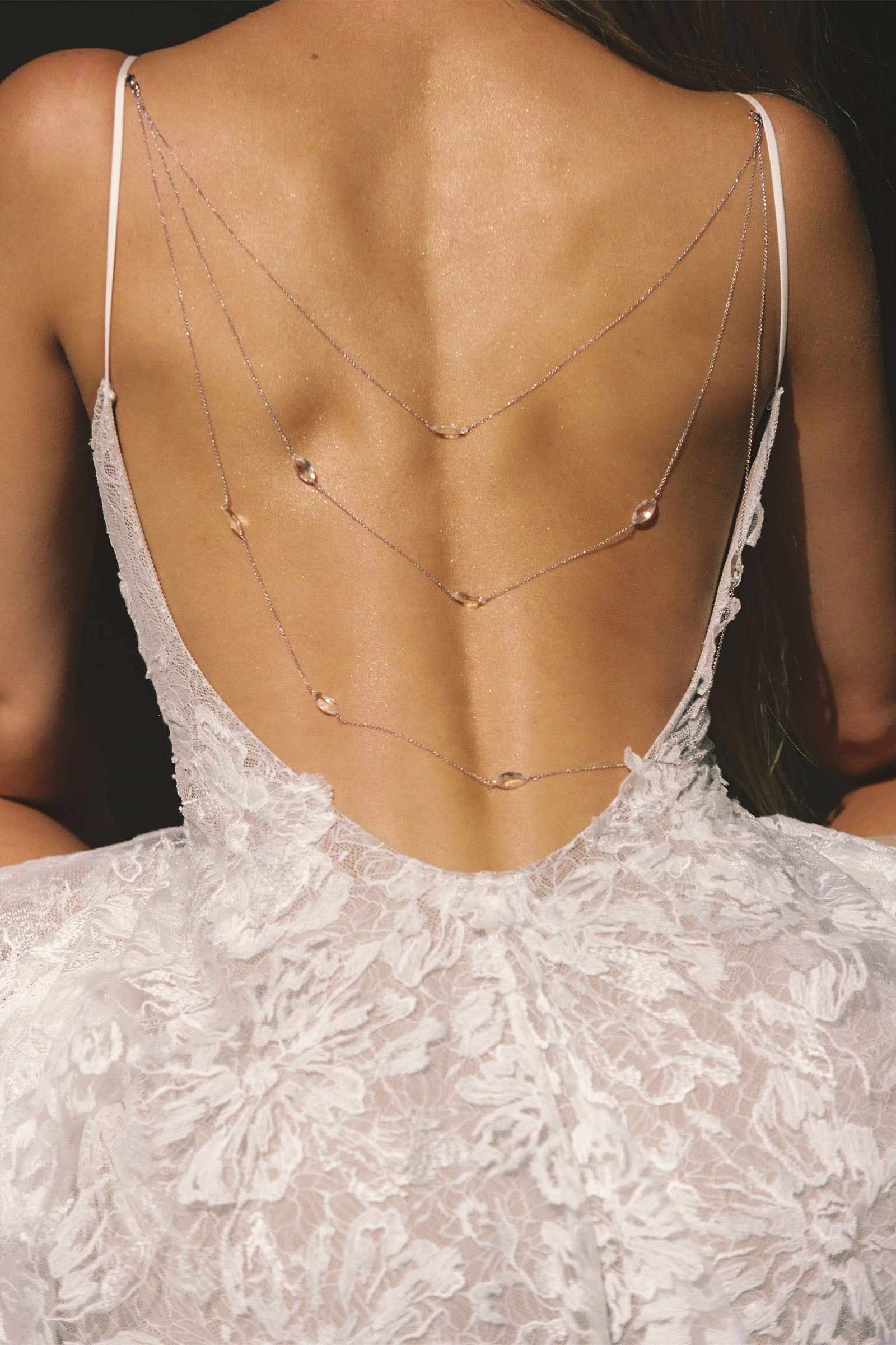woman wearing a white lace backless dress with thin straps and delicate chain jewellery across her back_XS_