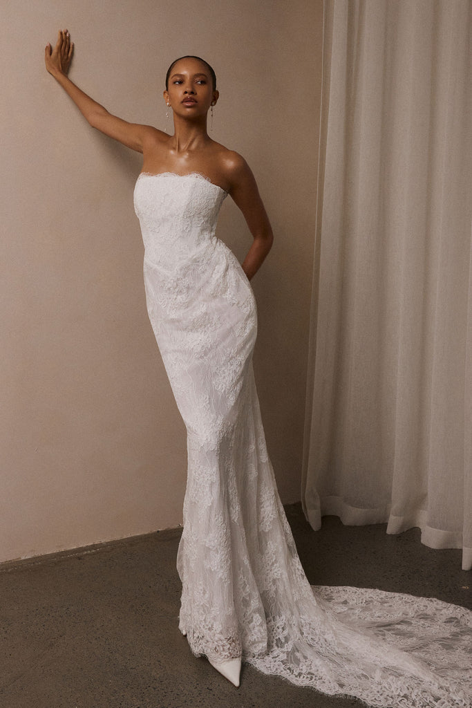 A woman wearing a strapless white lace wedding gown with a long train