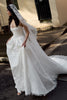 Woman in a white wedding dress with a long train and veil standing on a street.