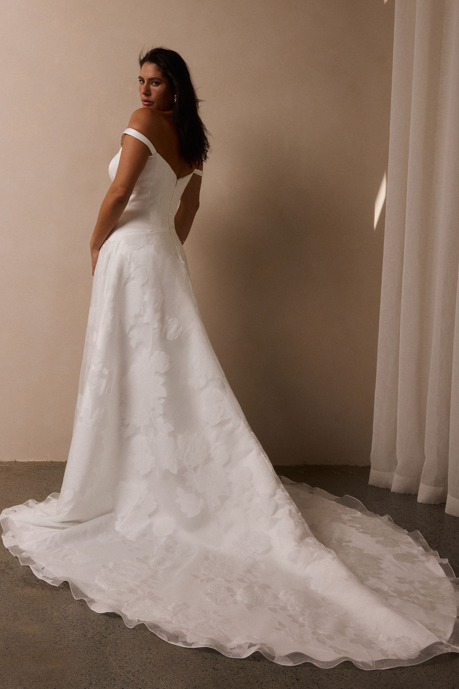 A woman wearing an off-the-shoulder white wedding dress with a fitted bodice and flowing skirt_L_