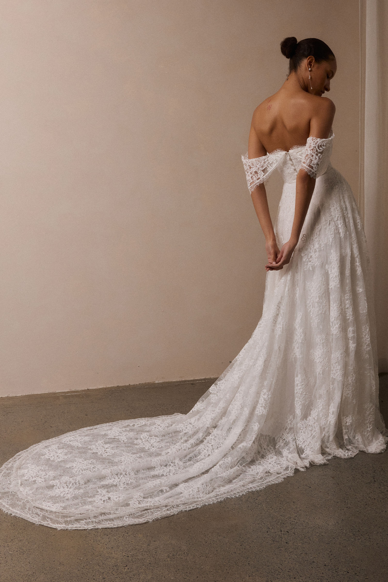 A woman wearing a white off-the-shoulder lace wedding gown with a deep V neckline and a full layered skirt_XS_