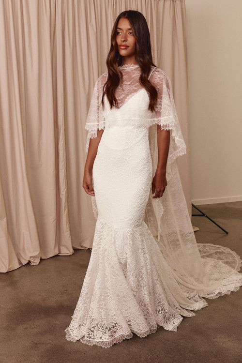 Woman wearing a white lace wedding dress with a sheer overlay cape