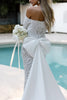 Woman in a white lace wedding dress and bow holding a bouquet by a pool