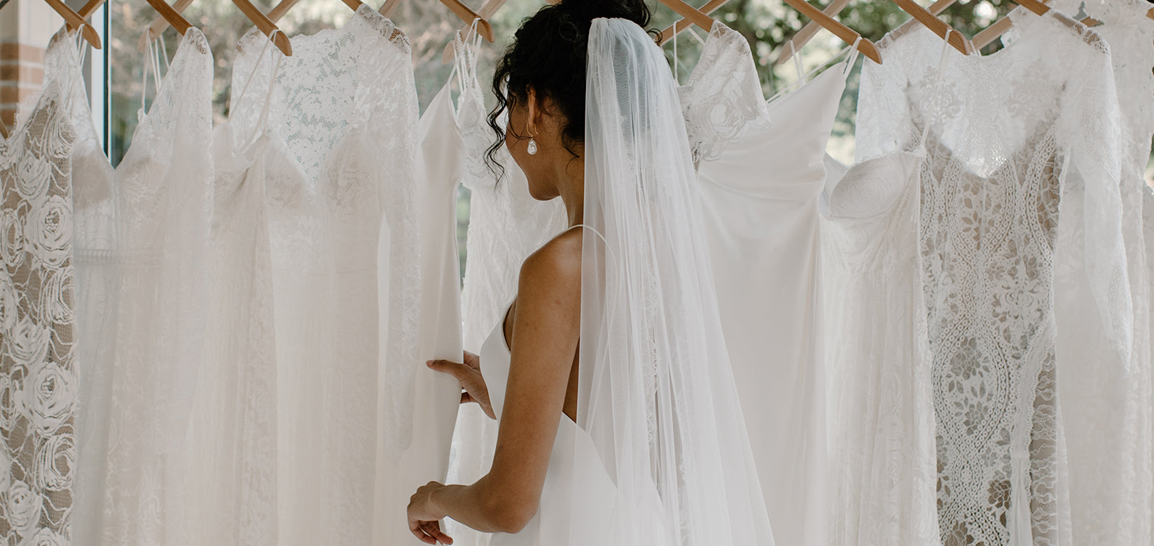 bride wearing wedding dress looking at a rack of wedding dresses